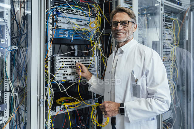 Sorridente uomo maturo collegare ricetrasmettitore su cavo in fibra ottica in data center — Foto stock