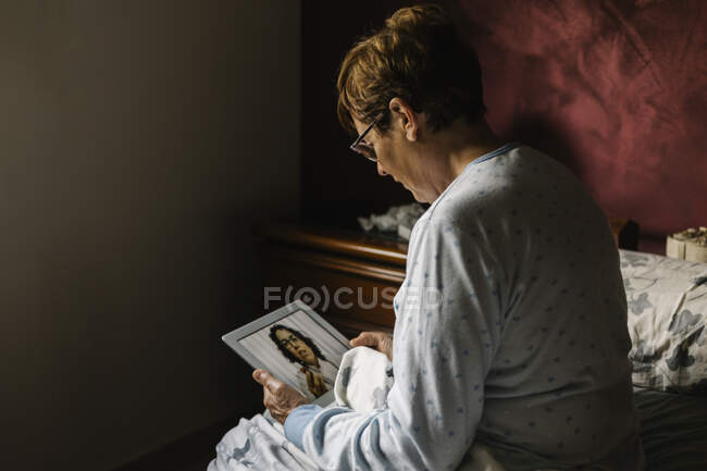 Старша жінка у спальні обговорює з лікарем відеодзвінок. — стокове фото