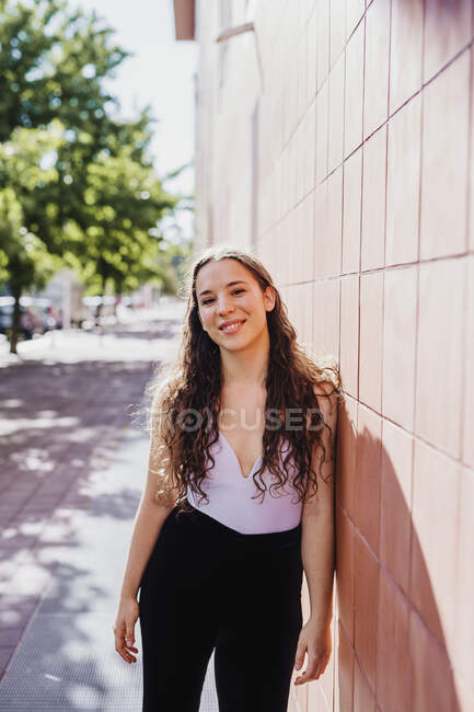 Feliz mujer deportiva apoyada en la pared de baldosas durante el día soleado - foto de stock