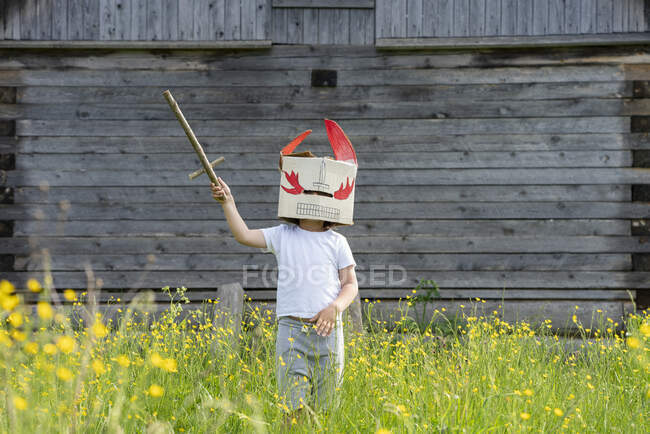 Junge mit Maske hält Spielzeugschwert in der Hand, während er inmitten von Pflanzen vor Hütte steht — Stockfoto
