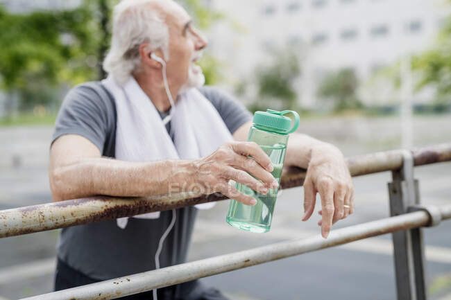 Старший чоловік тримає пляшку, слухаючи музику, стоячи на перилах у місті — стокове фото