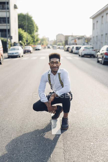 Портрет уверенного стильного молодого человека, приседающего на улице в городе — стоковое фото