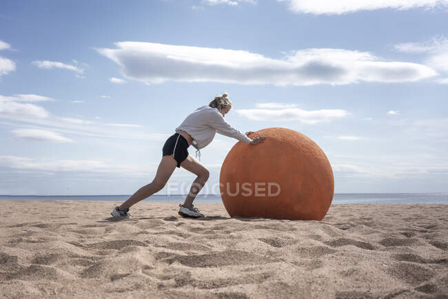 Молода жінка котиться оранжевим каменем на пляжі. — стокове фото