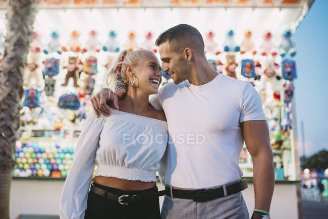 Романтичный парень смотрит на счастливую женщину, стоя напротив стойла в парке аттракционов — стоковое фото