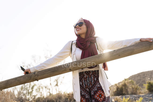 Улыбающаяся молодая туристка в хиджабе, опирающаяся на деревянные перила — стоковое фото