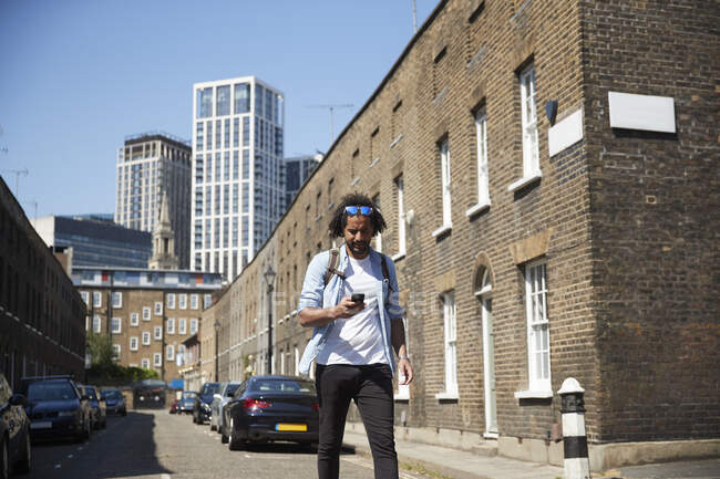 Young man walking on residential street looking at mobile phone, Londra, Regno Unito — Foto stock