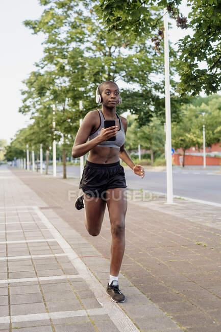 Женщина-атлет слушает музыку во время бега по тропинке в городе — стоковое фото