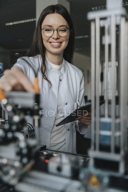 Cientista feminina sorridente segurando tablet digital trabalhando em laboratório na fábrica — Fotografia de Stock
