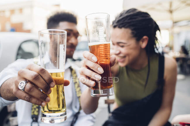 Felice giovane coppia clinking bicchieri di birra all'aperto in un bar — Foto stock