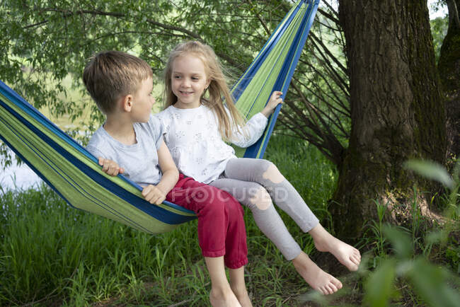 Ragazza parlando con ragazzo mentre seduto su amaca nella foresta — Foto stock
