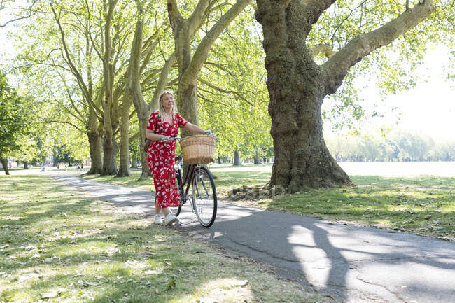 Mujer pensativa caminando con bicicleta en el sendero en el parque público - foto de stock