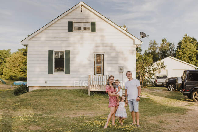 Portrait of smiling parents with two daughters standing in front of their home — Stock Photo