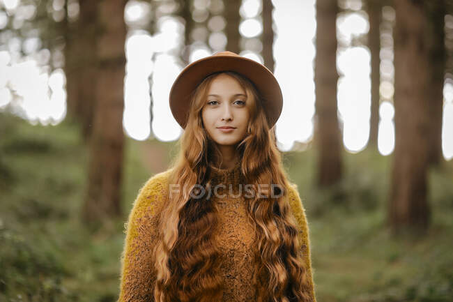 Bella donna con i capelli lunghi che indossa cappello in piedi nella foresta — Foto stock