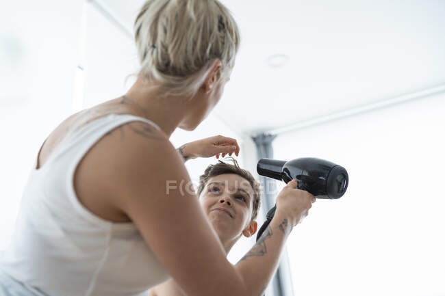 Жінка - перукар висушує хлопчаче волосся вдома. — стокове фото