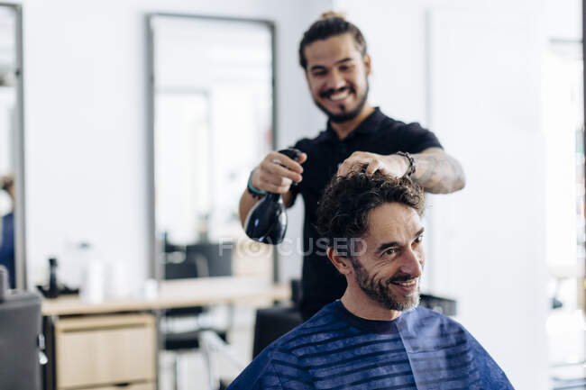 Glücklicher Friseur sprüht im Salon Wasser auf Männerfrisur — Stockfoto