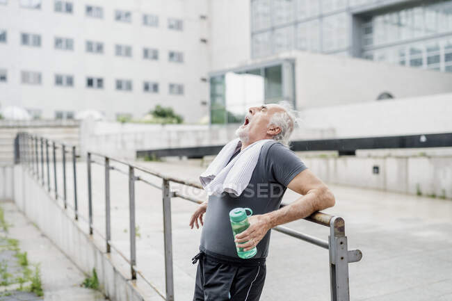 Müder Senior mit gähnender Flasche am Geländer in der Stadt — Stockfoto