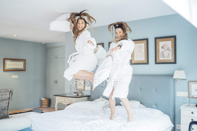 Весёлые сёстры-близнецы прыгают на кровати в гостиничном номере — стоковое фото