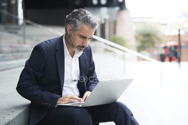 Businessman working on laptop in city - foto de stock