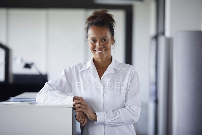 Портрет улыбающейся деловой женщины, опирающейся на прилавок в современном офисе — стоковое фото
