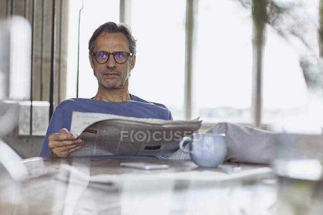 Hombre mayor sentado a la mesa en un loft periódico de lectura plana - foto de stock