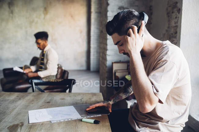 Креативный молодой бизнесмен с наушниками и смартфоном в лофт-офисе — стоковое фото