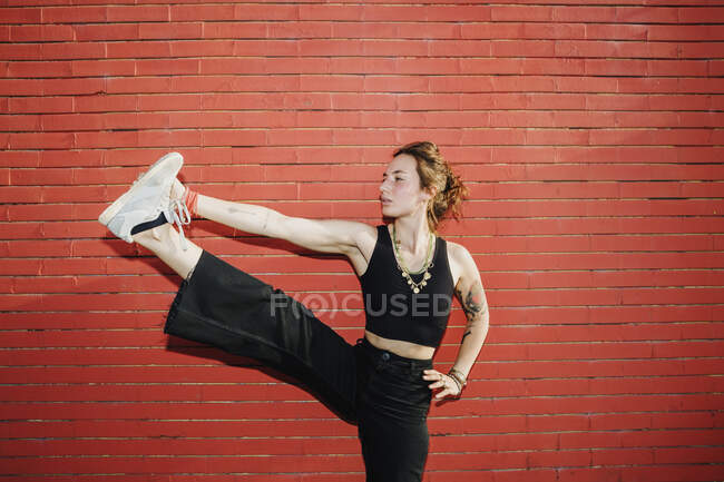 Mulher bonita esticando a perna contra a parede vermelha — Fotografia de Stock