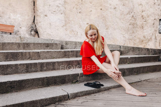 Femme portant une robe rouge assise sur les marches et massant son pied — Photo de stock