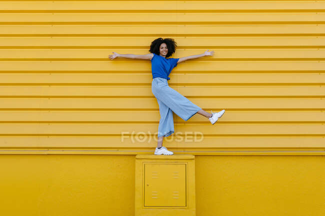 Щаслива молода жінка балансує на платформі перед жовтою стіною. — стокове фото