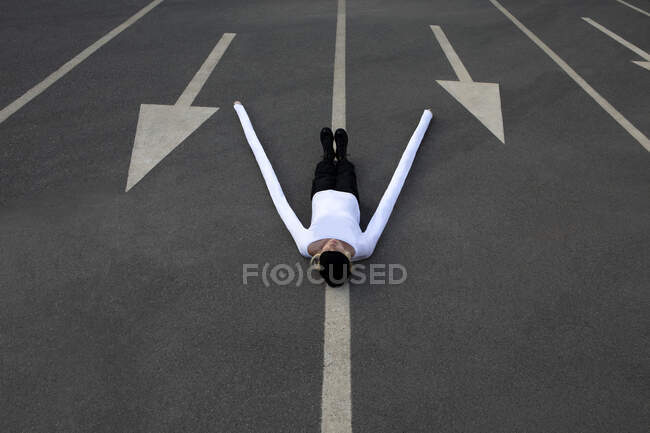 Donna con lunghe mani artificiali sdraiata tra i simboli freccia sulla strada — Foto stock
