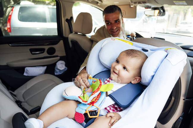 Отец закрепляет мальчика сидящего на детском сиденье в машине — стоковое фото