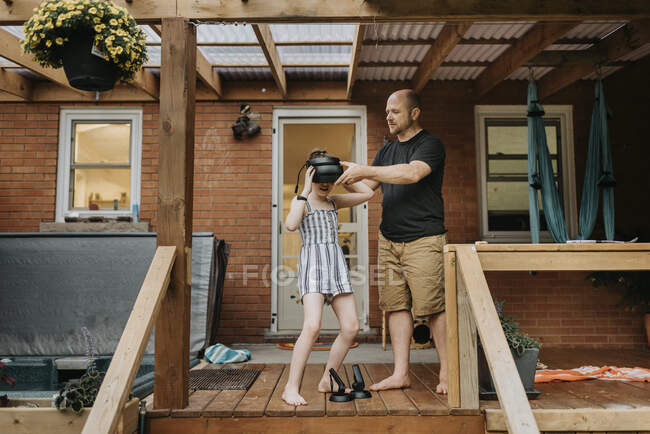 Батько носив імітатор віртуальної реальності дочці, стоячи біля будинку. — стокове фото