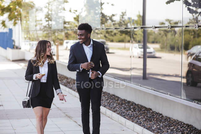 Professional coworkers discussing while walking on sidewalk in city — Stock Photo