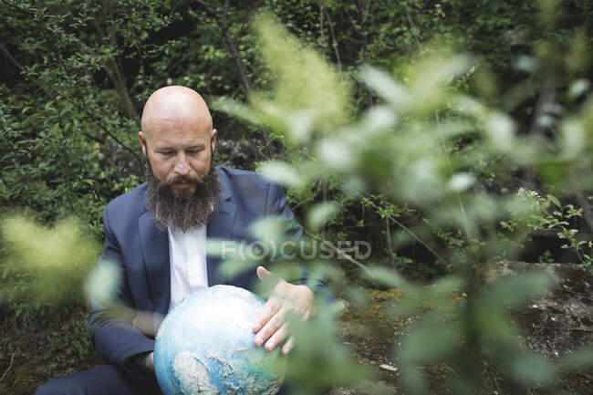 Calvo barbudo empresario sosteniendo globo mientras está sentado en el bosque - foto de stock