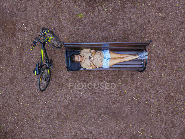 Aerial view of woman using smart phone while lying on park bench — Stock Photo