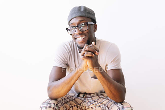 Homme souriant assis avec les mains serrées sur fond blanc — Photo de stock