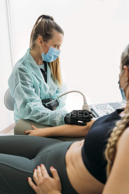 Doctor wearing face mask examining sportswoman with ultrasound scanner — Stock Photo