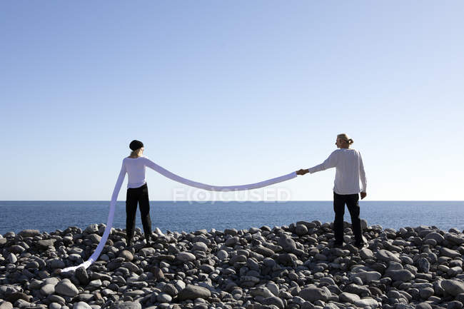 Donna con lunghe braccia artificiali che tengono la mano dell'uomo in spiaggia contro il cielo limpido — Foto stock