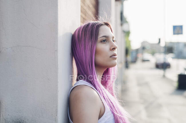 Portrait of a stylish young woman with pink hair leaning against a wall in the city — Stock Photo