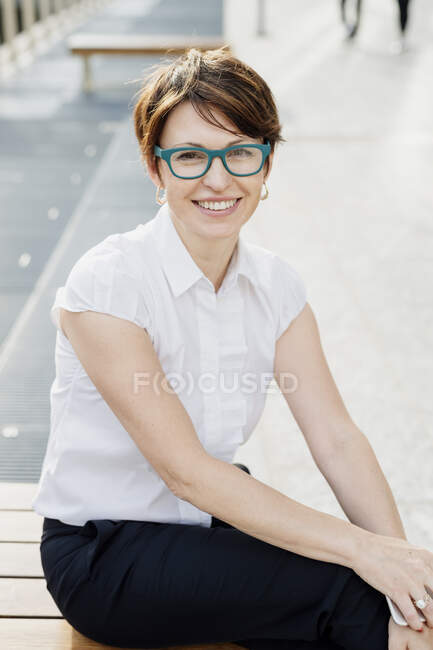 Lächelnde Berufstätige mit Brille sitzen in der Stadt auf dem Sitz — Stockfoto