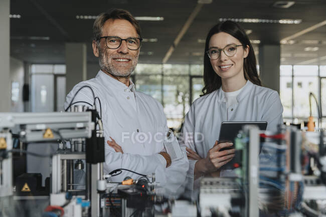 Улыбающиеся ученые мужского и женского пола, стоящие у машин в лаборатории — стоковое фото