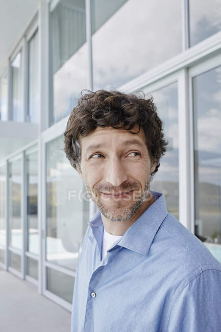 Portrait of a smiling man outside a house looking sideways — Stock Photo