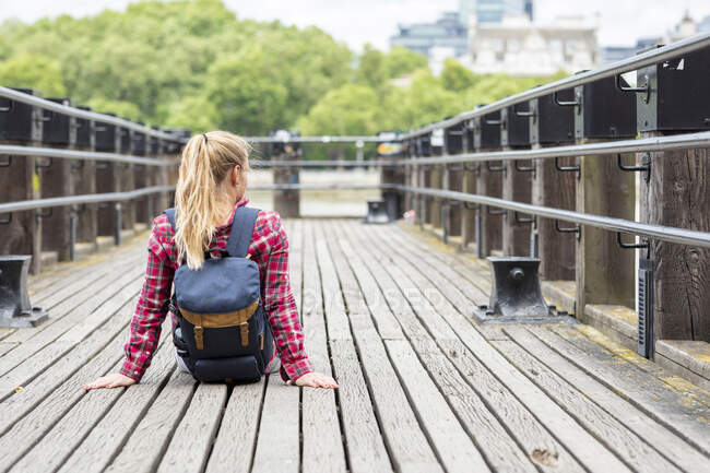 Mitte erwachsene Frau mit Rucksack sitzt auf Brücke in der Stadt — Stockfoto