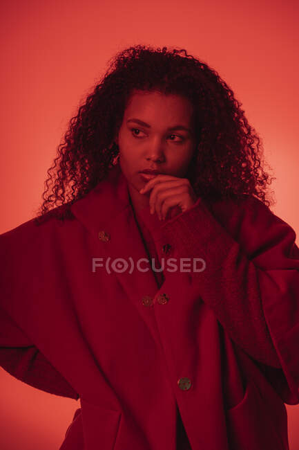 Продумана молода жінка в червоному пальто, що стоїть на помаранчевому фоні — стокове фото