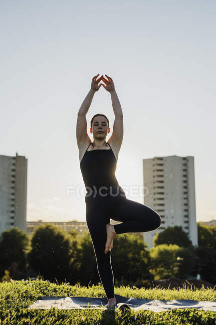 Young woman practicing yoga in tree pose at city park against clear sky — Stock Photo
