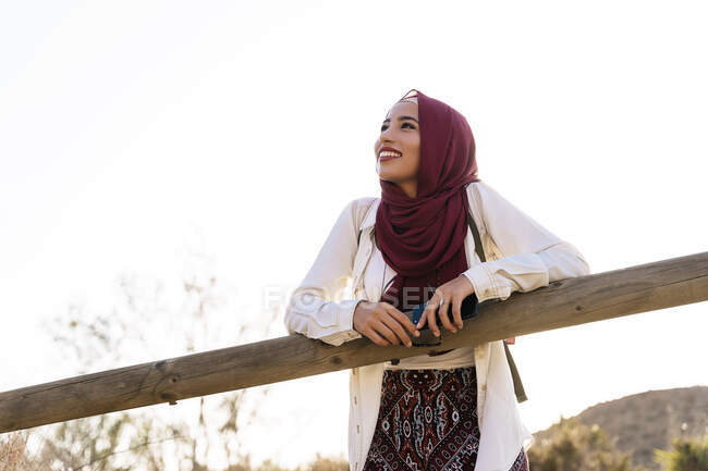 Smiling young tourist woman wearing Hijab leaning on wooden railing — Stock Photo