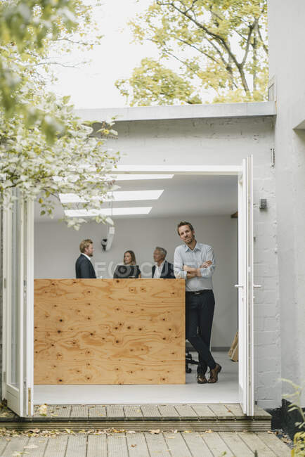Businessman standing in open office door, people working in background — Stock Photo
