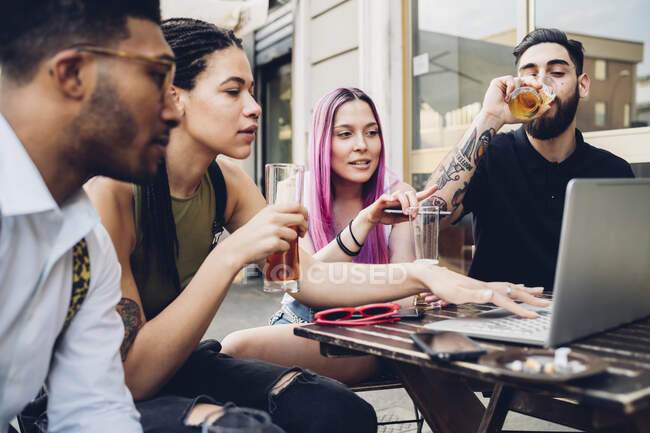 Friends drinking beer and using laptop outdoors at a bar — Stock Photo