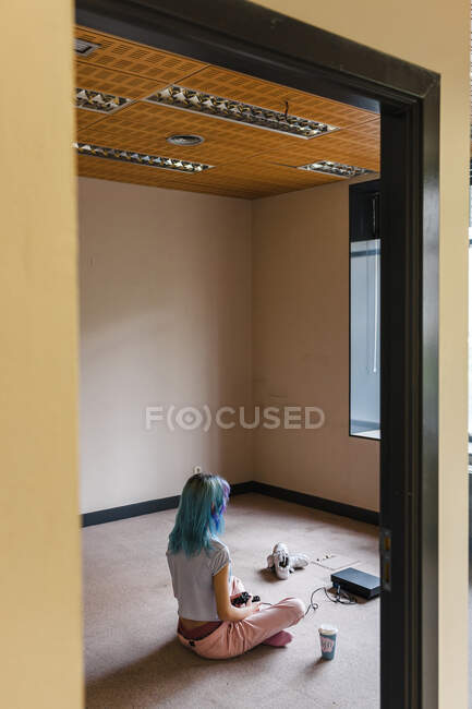 Mujer de pelo azul de moda jugando videojuego en el suelo en casa - foto de stock