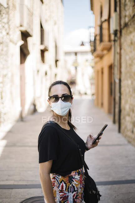 Женщина в защитном костюме просит и пользуется смартфоном в переулке — стоковое фото