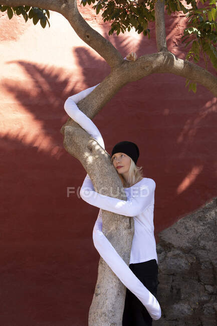 Donna riflessivo con mani lunghe artificiali abbracciando tronco d'albero contro parete — Foto stock